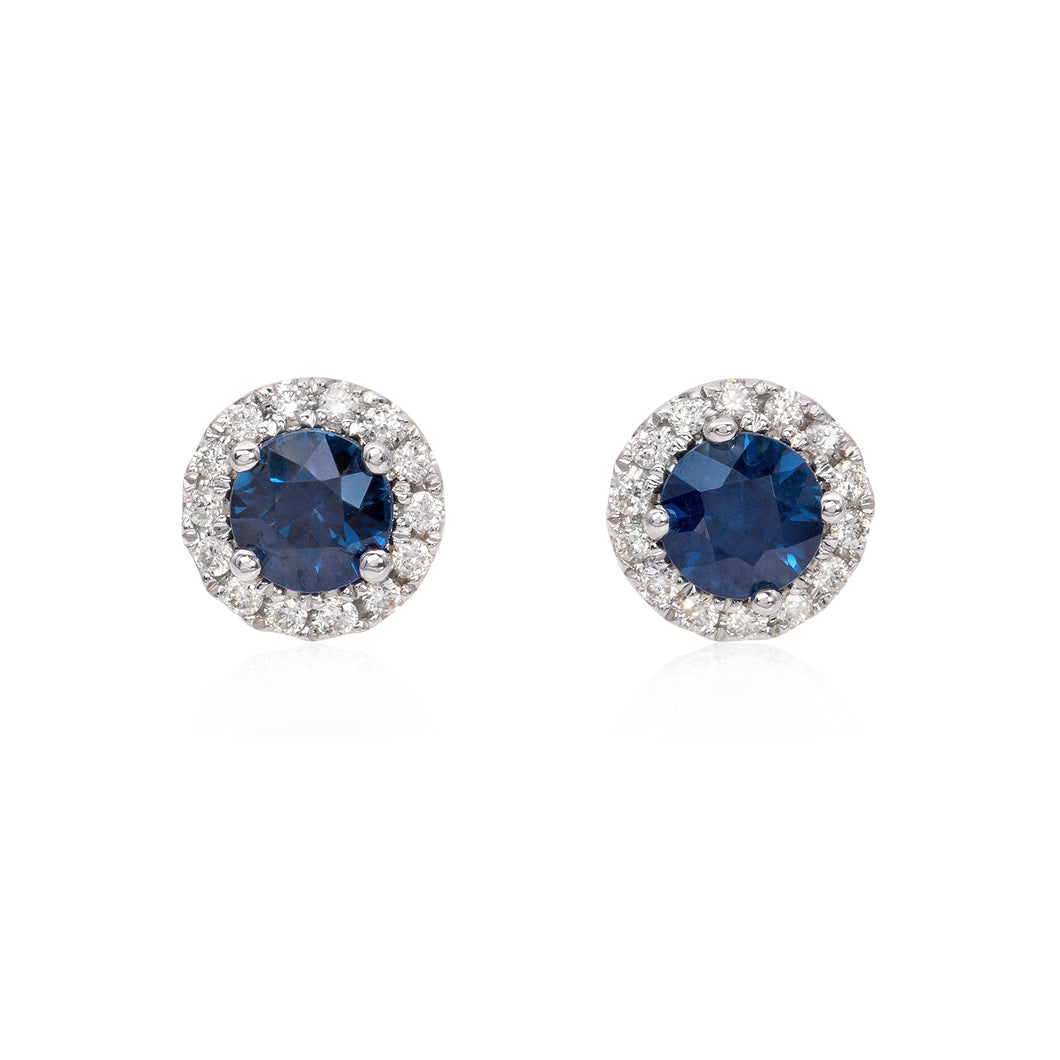 14k white gold diamond and sapphire button earrings featuring 28 round brilliant cut diamonds weighing .12 carats total of F color, VS2 clarity, and of excellent cut and brilliance. Earrings also feature 2 sapphires weighing .61 carats of excellent cut, hue, and even color distribution.