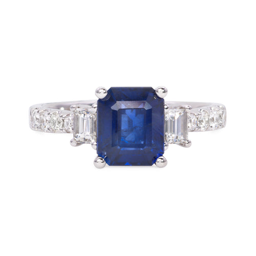 14k white gold diamond and sapphire ring featuring 2 emerald cut diamonds weighing .31 carats total, 8 round brilliant cut diamonds weighing .26 carats total, of excellent cut and brilliance. Center is a cushion cut sapphire weighing 2.41 carats of excellent cut, hue, and even color distribution.