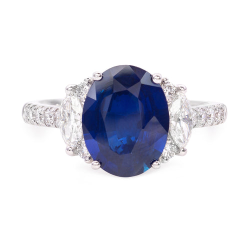 18k white gold diamond and sapphire ring featuring 2 marquise cut diamonds weighing .51 carats total, and 14 round brilliant cut diamonds weighing .32 carats total of F color, VS2 clarity, and of excellent cut and brilliance. Center is an oval brilliant cut sapphire weighing 3.02 carats of excellent cut, hue, and even color distribution.